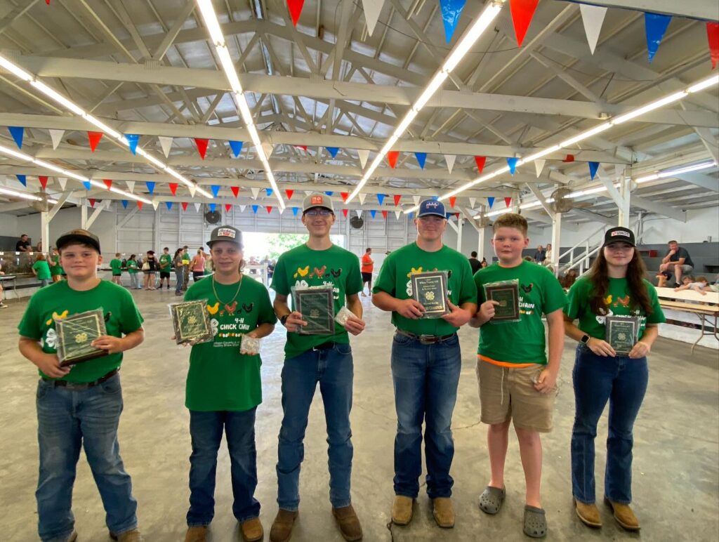 youth holding plaques, ribbons and belt buckles acknowledging winning poultry breeds.