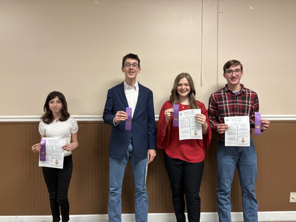 Four youth smiling and holding 4-H purple ribbons